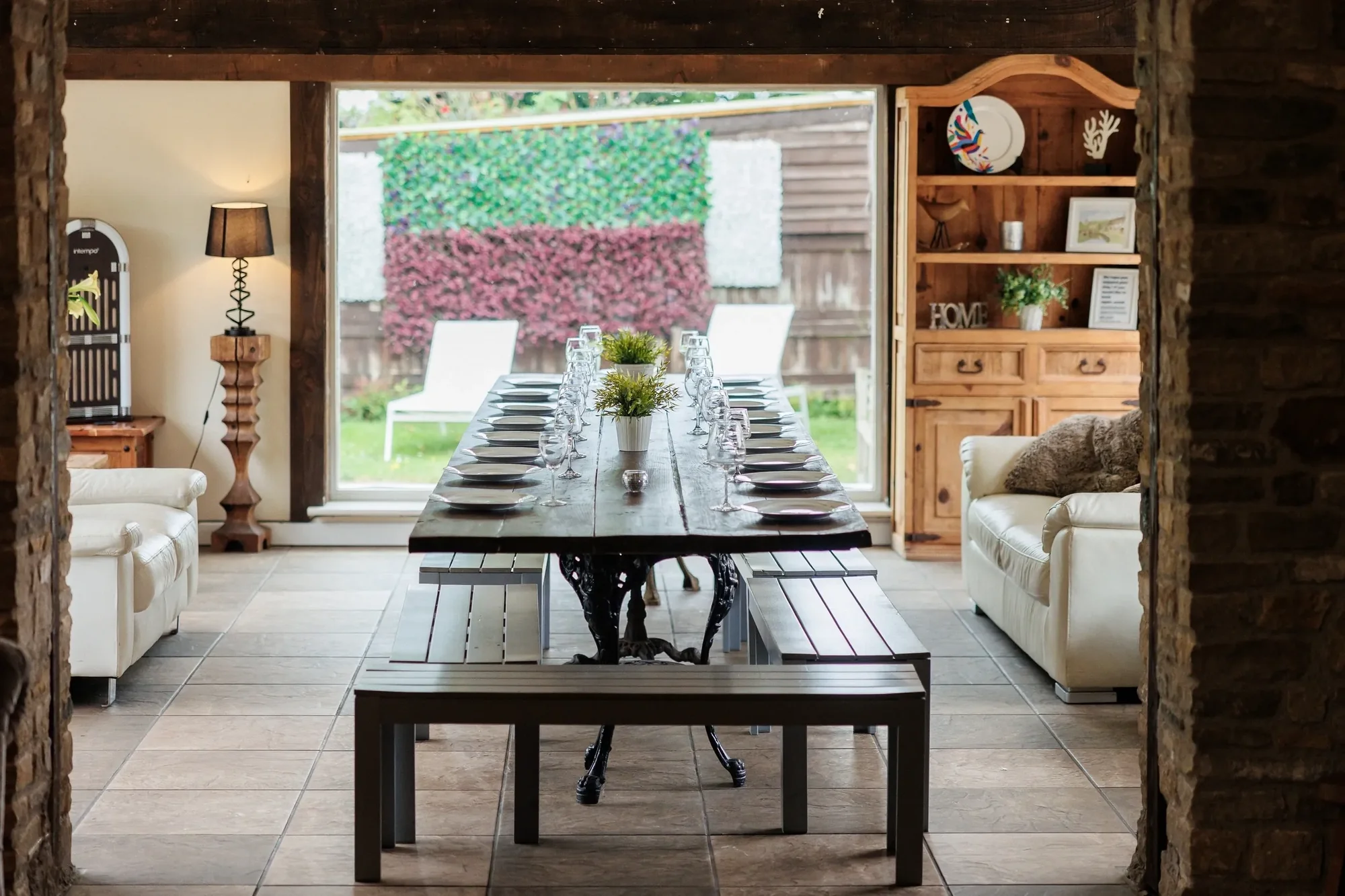 Barn dining room with long iron-framed table and benches, French doors to the garden and side seating area