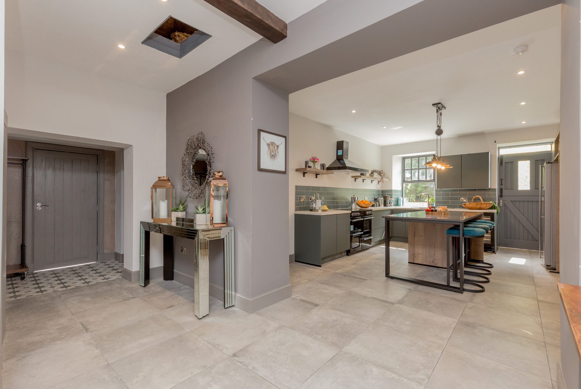 Open entrance hall flowing into a sage shaker kitchen with island, mirrored console and Highland cow print