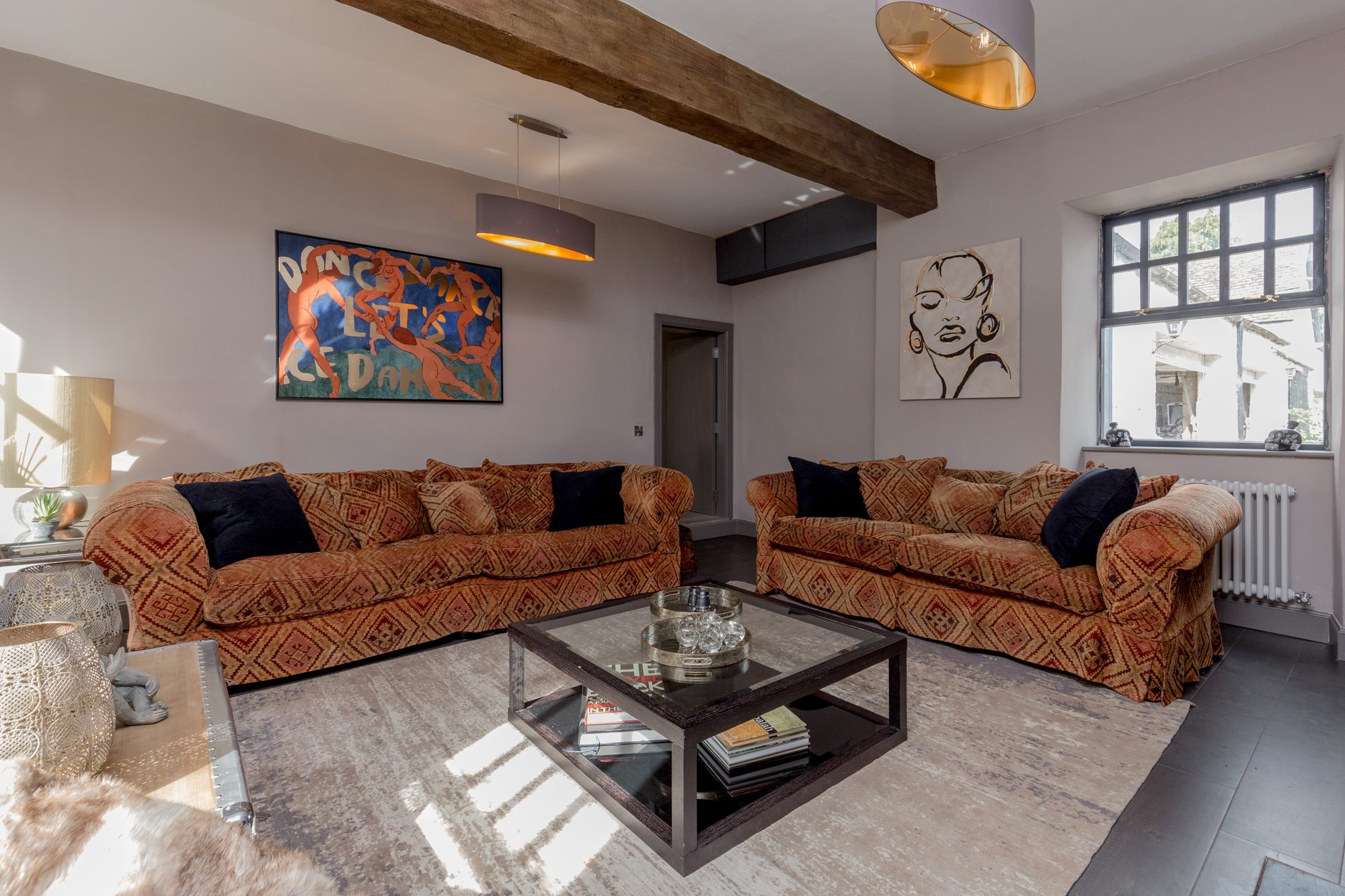 Lounge with twin ochre patterned sofas, exposed oak beam and a colourful figurative painting