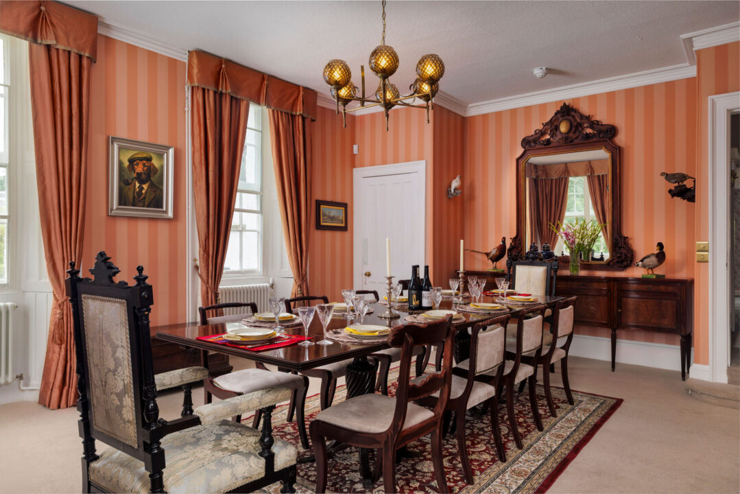 The formal dining room with striped walls, a long mahogany table laid for dinner and a chandelier