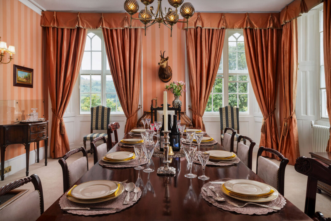 The dining table dressed with candles and glassware, Gothic windows onto the valley behind