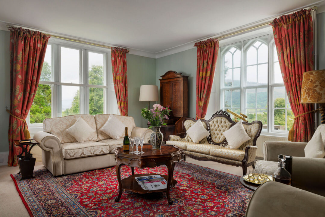 The drawing room with cream and gilt sofas, red curtains and Gothic windows looking onto the hills