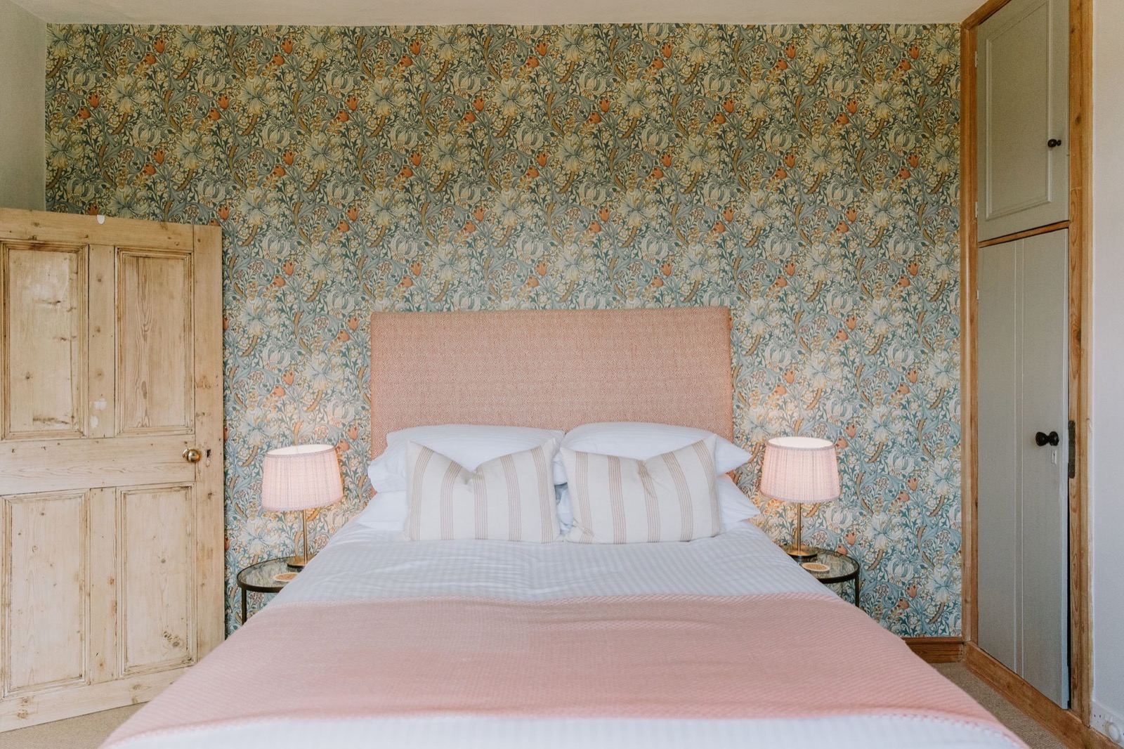 Bedroom with William Morris floral wallpaper, pink upholstered headboard and striped cushions, The Old Farmhouse