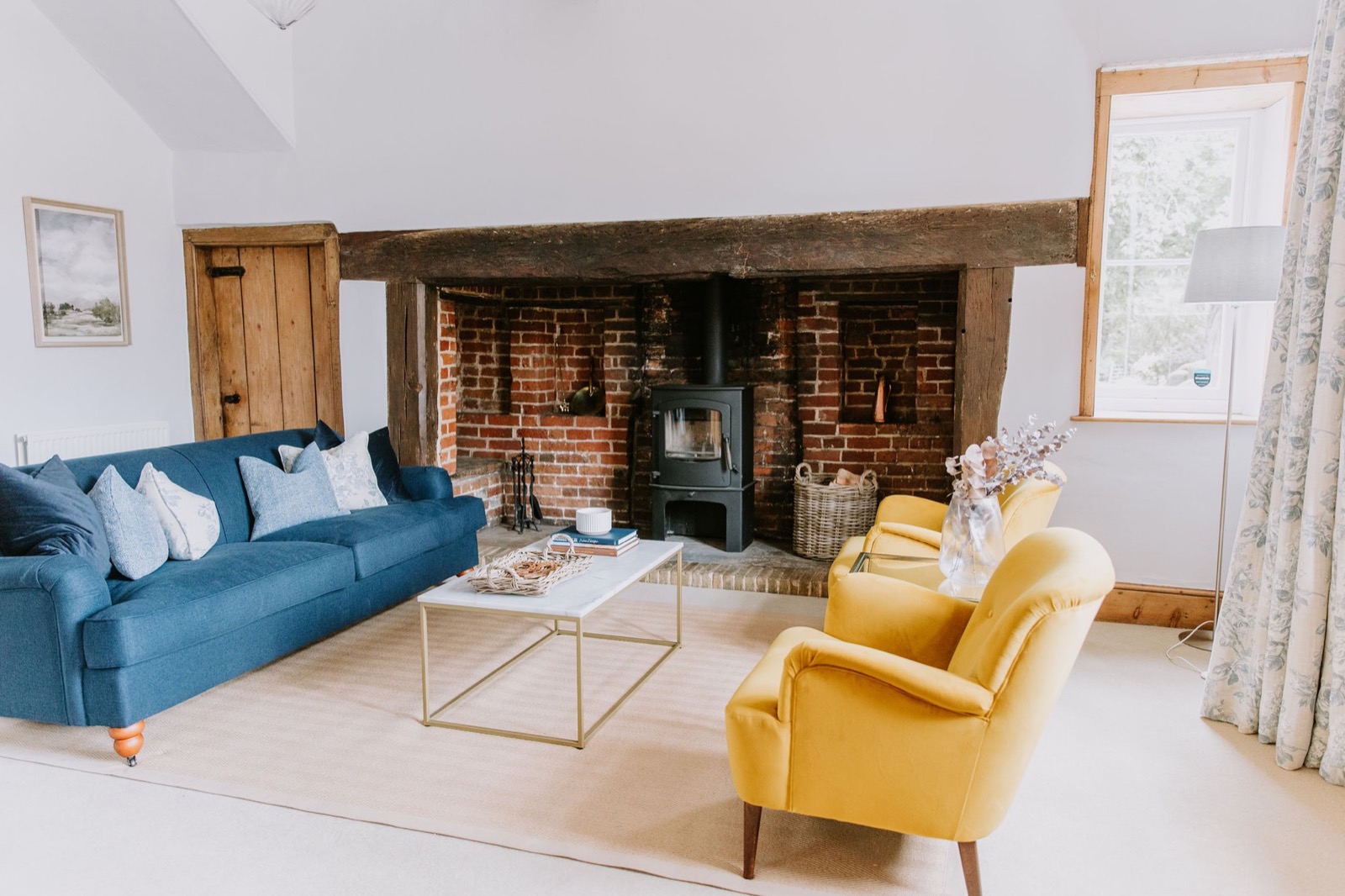 Living room with deep blue sofa, mustard armchairs and a log burner set into a brick inglenook, The Old Farmhouse