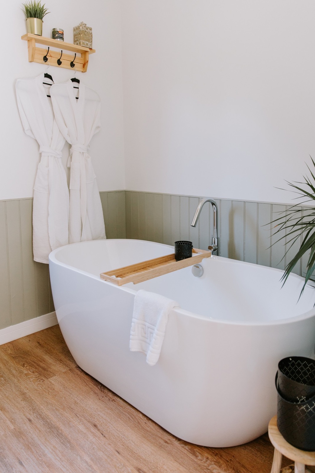 Freestanding bath with white robes hanging alongside and a sage panelled wall, The Wildflower Cabins