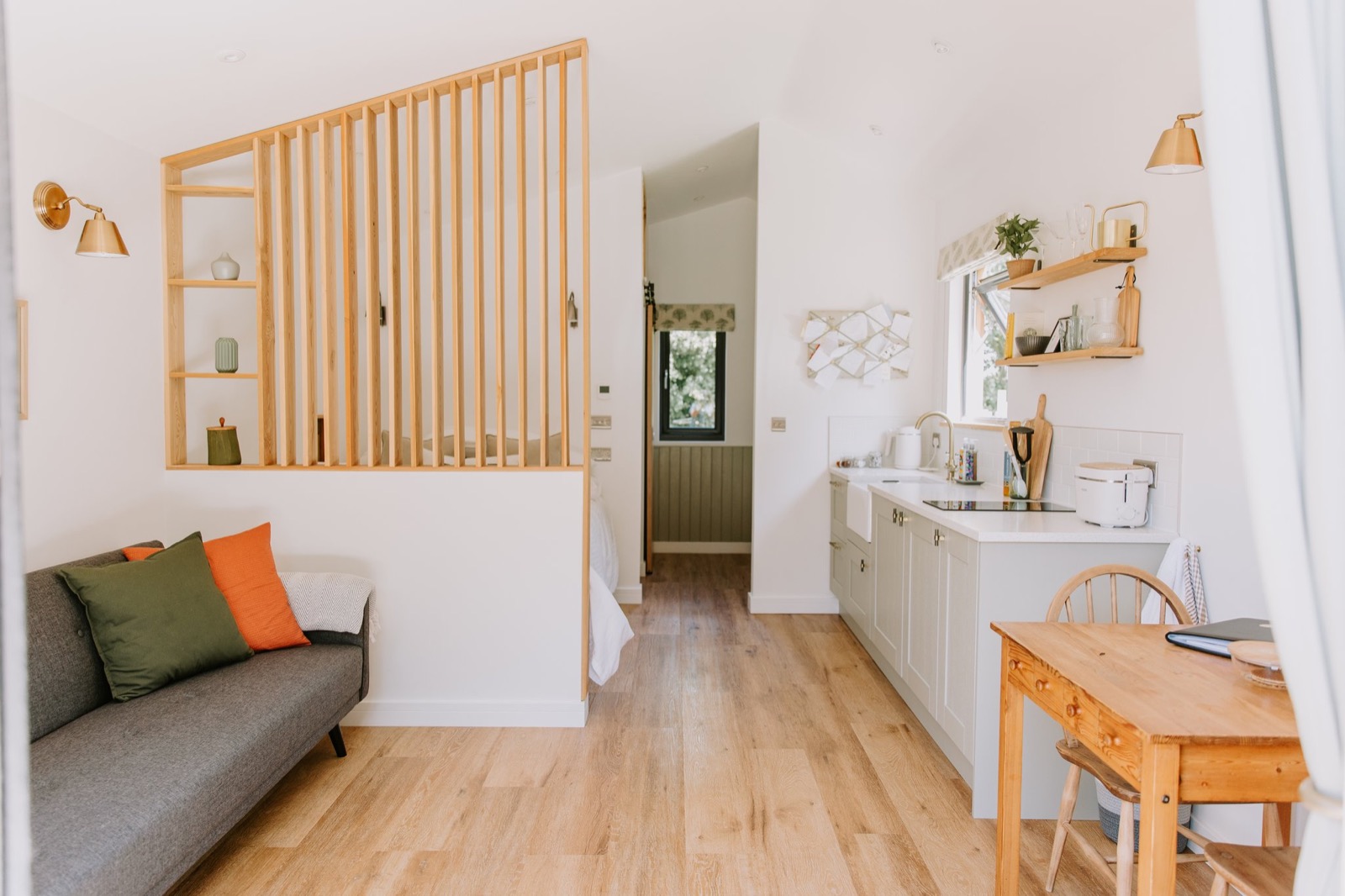 Open-plan cabin interior with a sofa, slatted oak screen, kitchen and dining table, The Wildflower Cabins