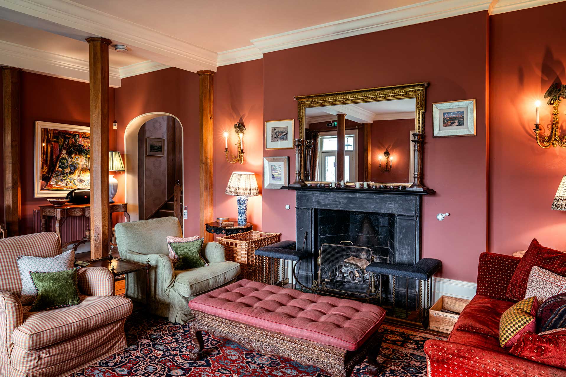 Wider view of the red drawing room with green armchair, pink ottoman and archway through to the library, The Country Social