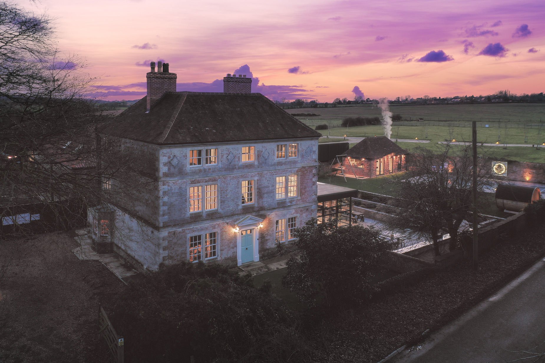 Three-storey Georgian stone house at sunset with pale-blue front door, pool and outbuilding lit, The Georgian Beauty