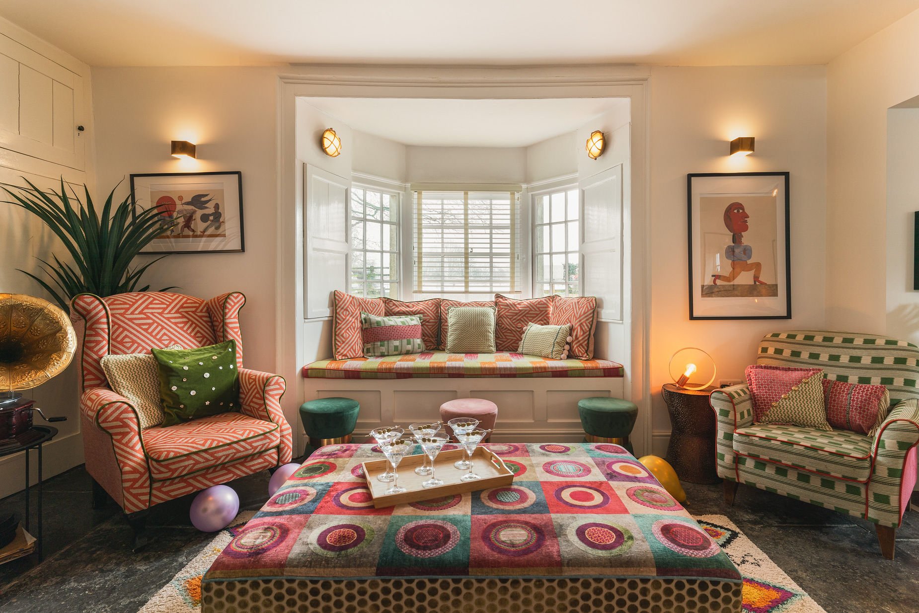 Maximalist sitting room with pink wing chair, green checked armchair and patchwork ottoman with martini glasses, The Georgian Beauty
