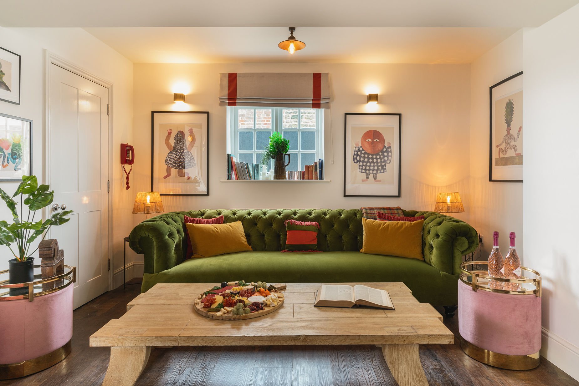Snug with green velvet chesterfield, mustard cushions, charcuterie board on chunky wood table and rose bottles on a pink velvet stool, The Georgian Beauty