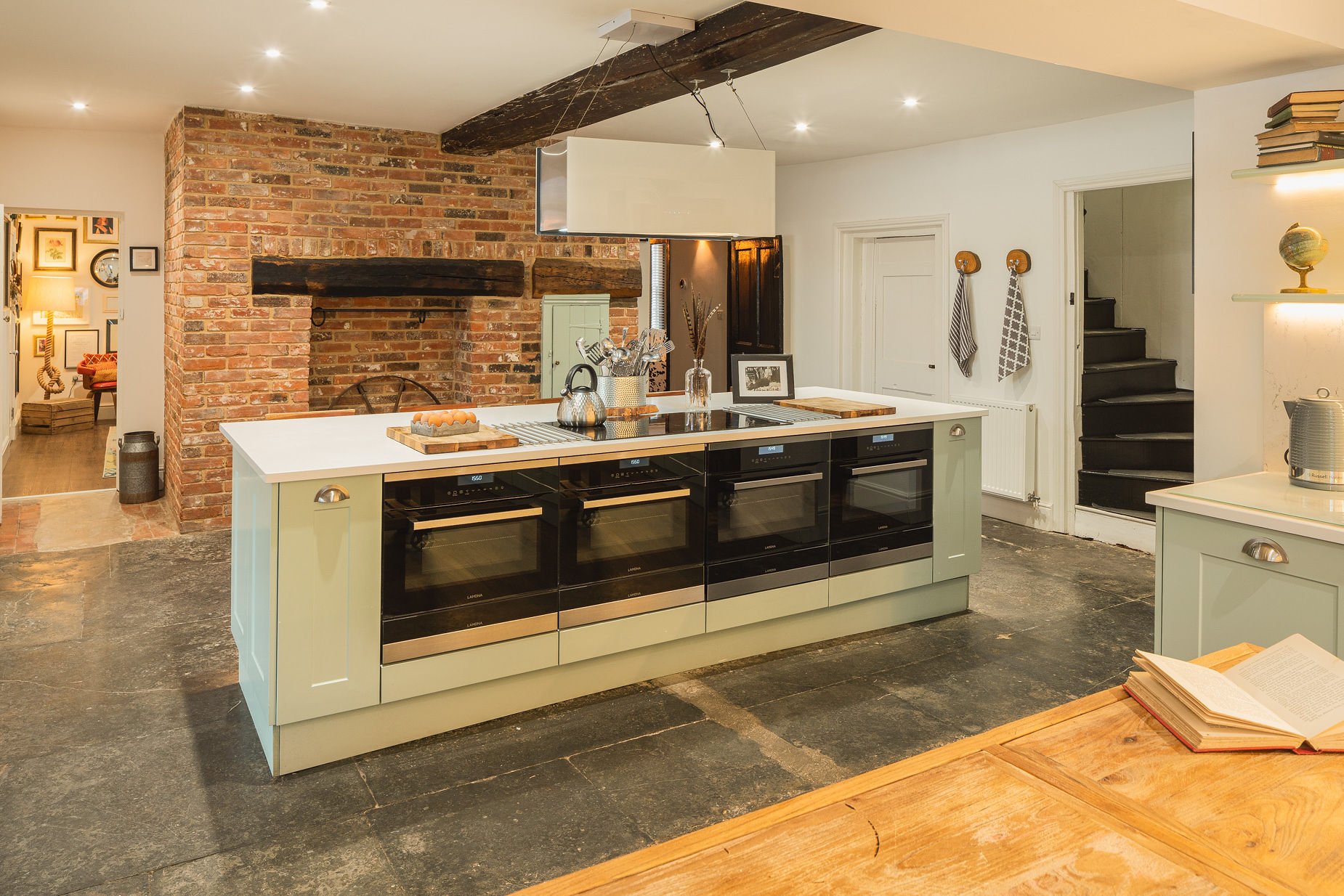 Sage-green kitchen island with row of ovens, exposed-brick hearth wall and slate floor, The Georgian Beauty