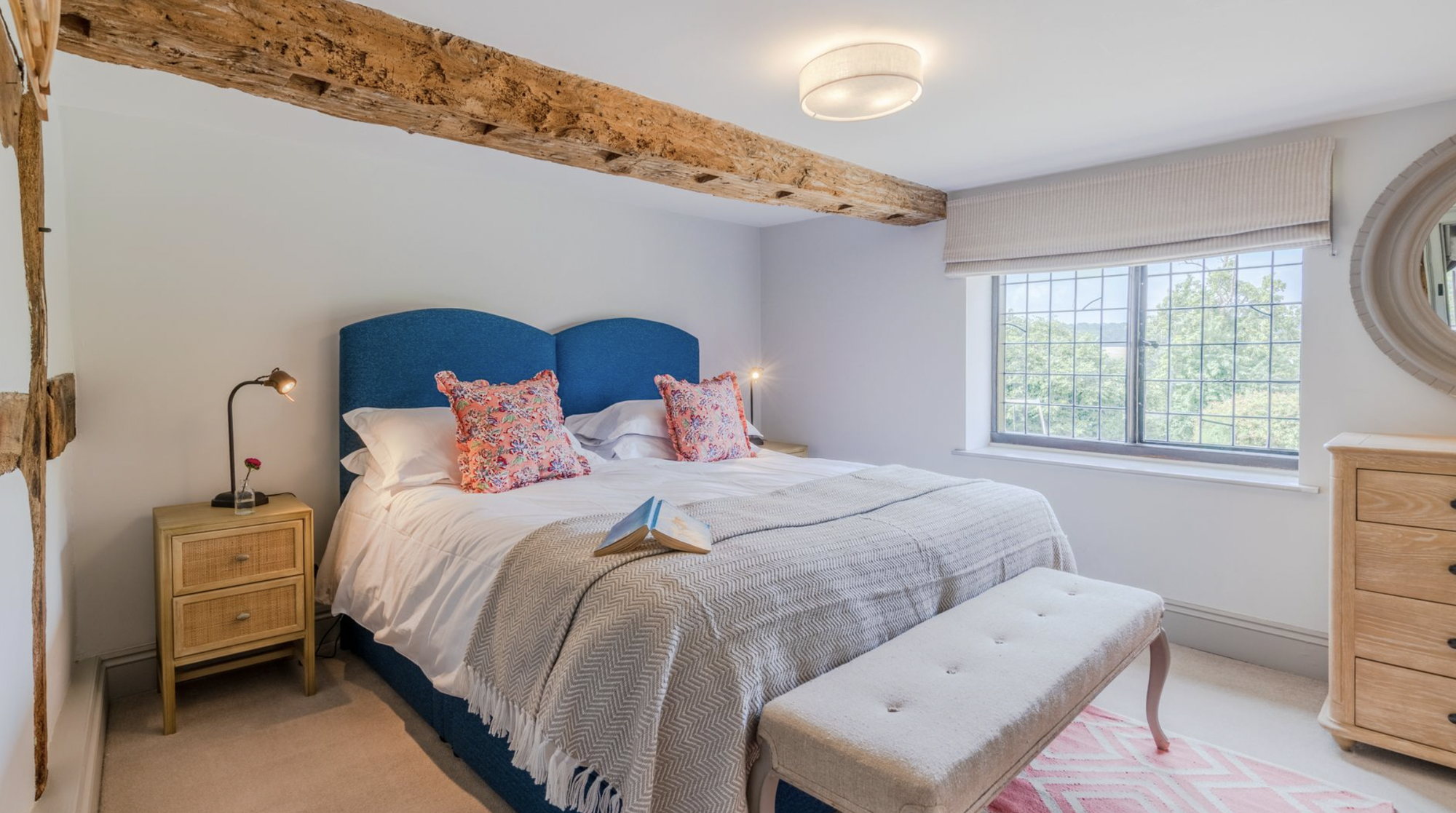 Bedroom with electric-blue headboard, oak ceiling beam and leaded window over the countryside