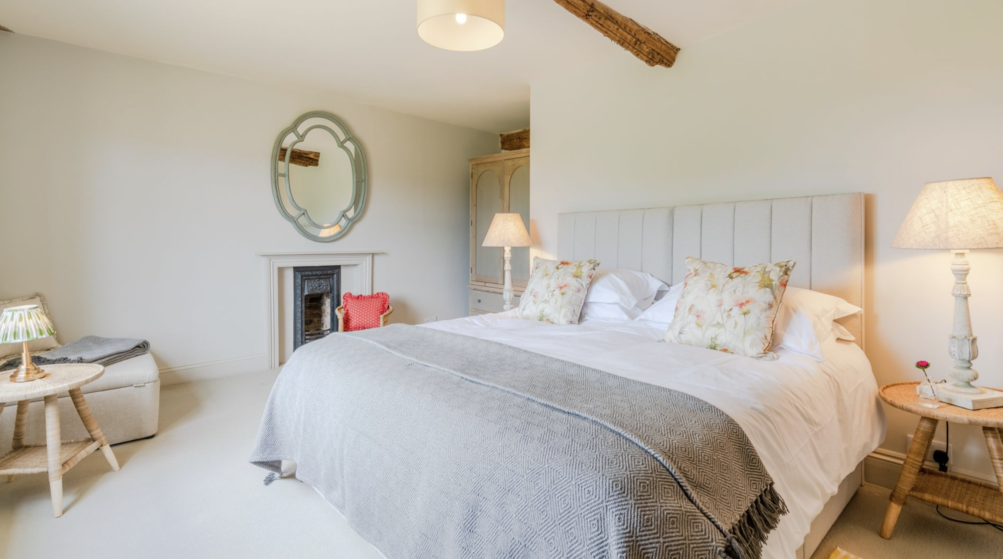 Neutral bedroom with channel-tufted upholstered headboard, small black fireplace and oval mirror