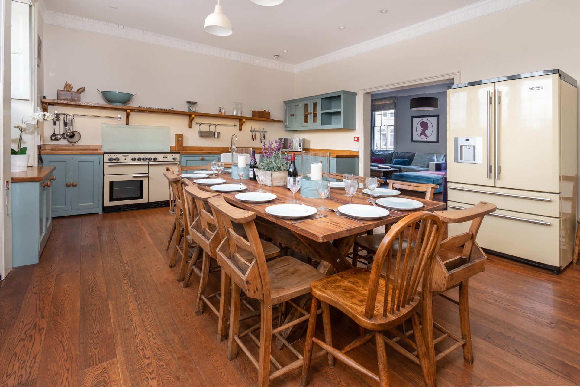 Kitchen and dining room with sage cabinets, a range cooker and the long farmhouse table set for fourteen