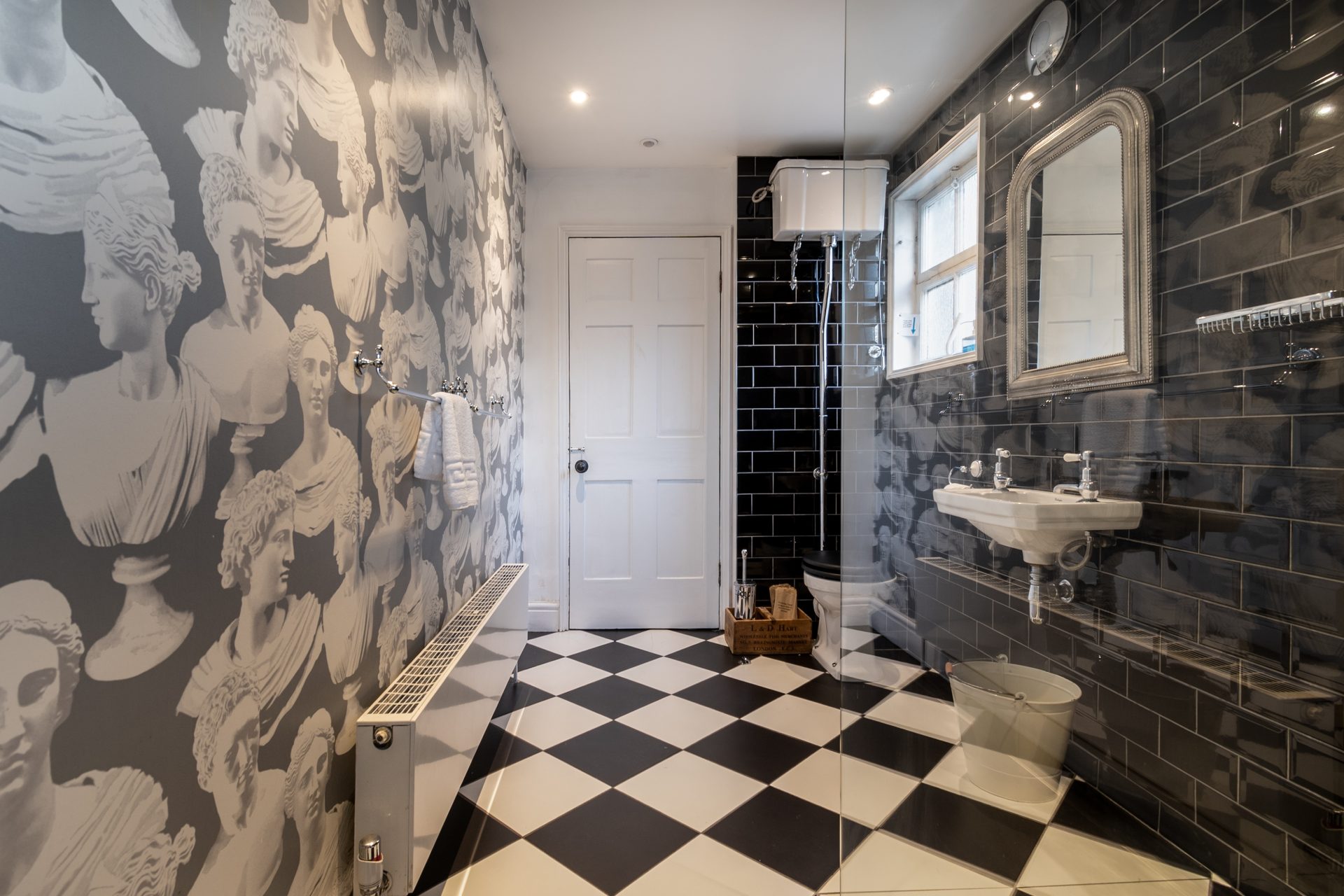Wet room with classical bust wallpaper, black metro tiles and a monochrome checkerboard floor