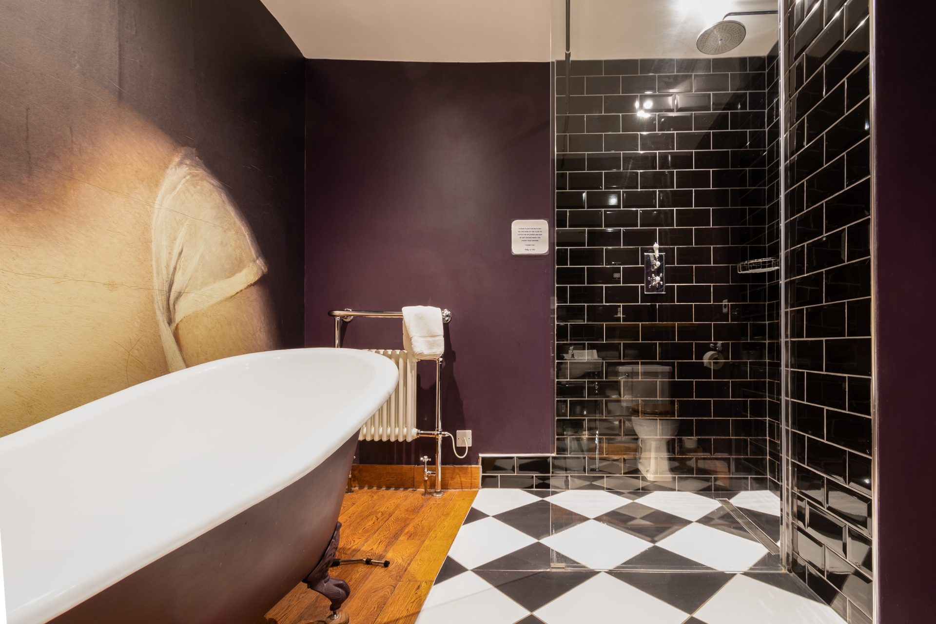Aubergine bathroom with classical portrait mural, clawfoot tub and black metro-tile walk-in shower