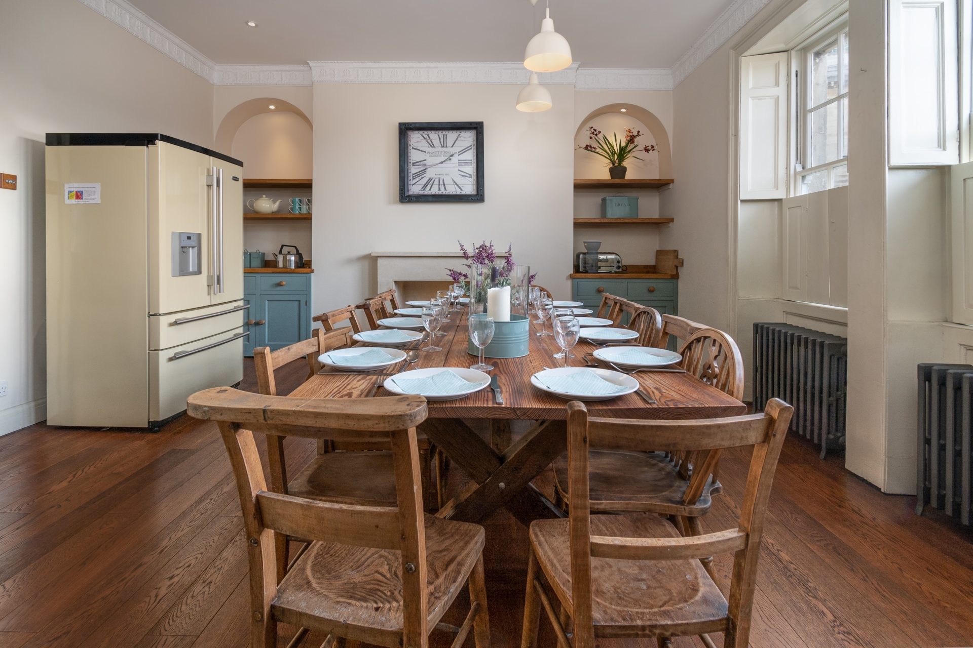 Dining room with cream Smeg fridge, long farmhouse table set for fourteen and a station wall clock