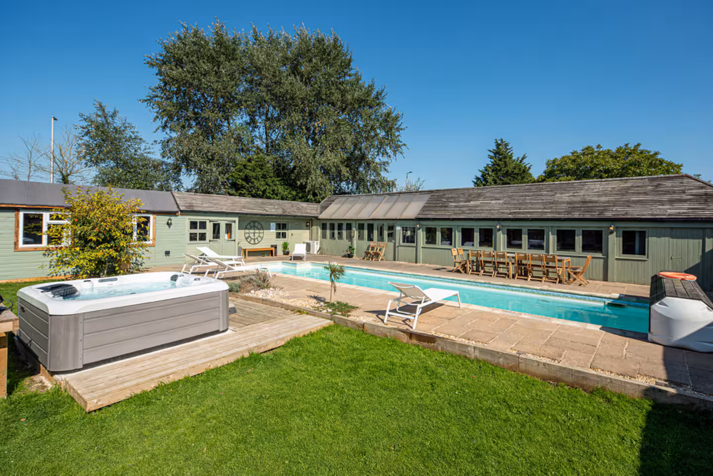 Side view of the pool and the white outdoor hot tub on the deck, with the green-roofed pool house running along the back