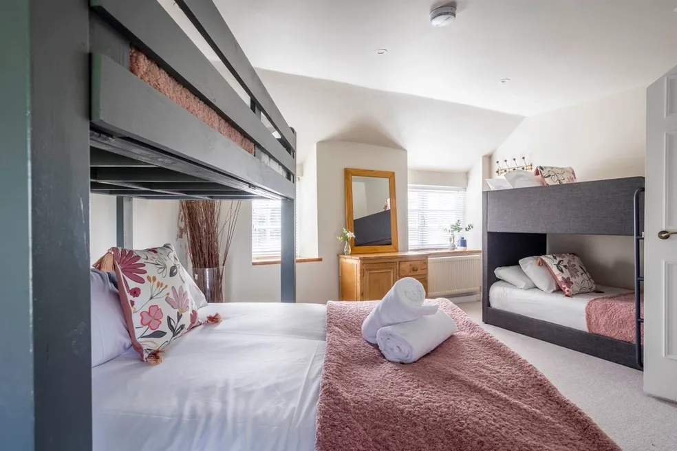 Bedroom with dark grey bunk frames either side of a double bed and a pink fluffy throw