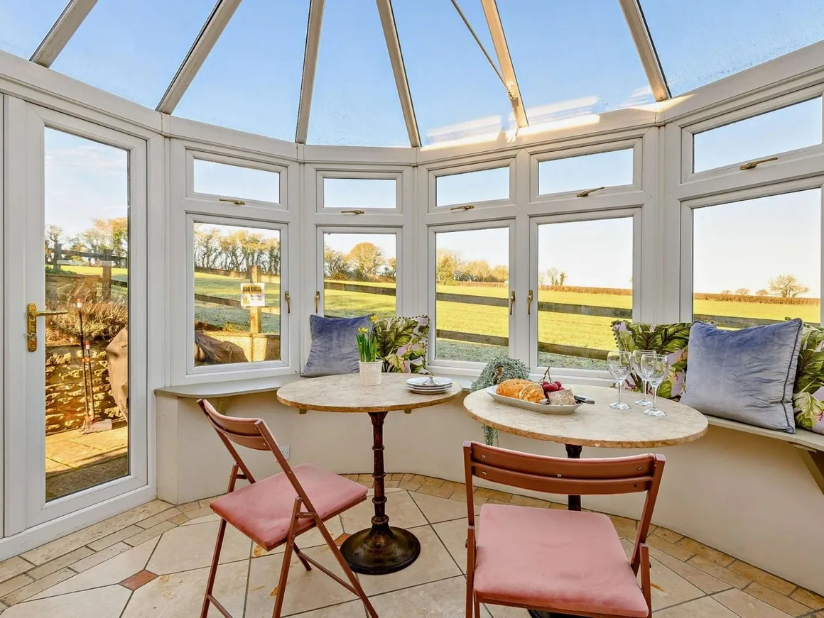 Octagonal glass conservatory with marble bistro tables, pink velvet chairs and farmland views