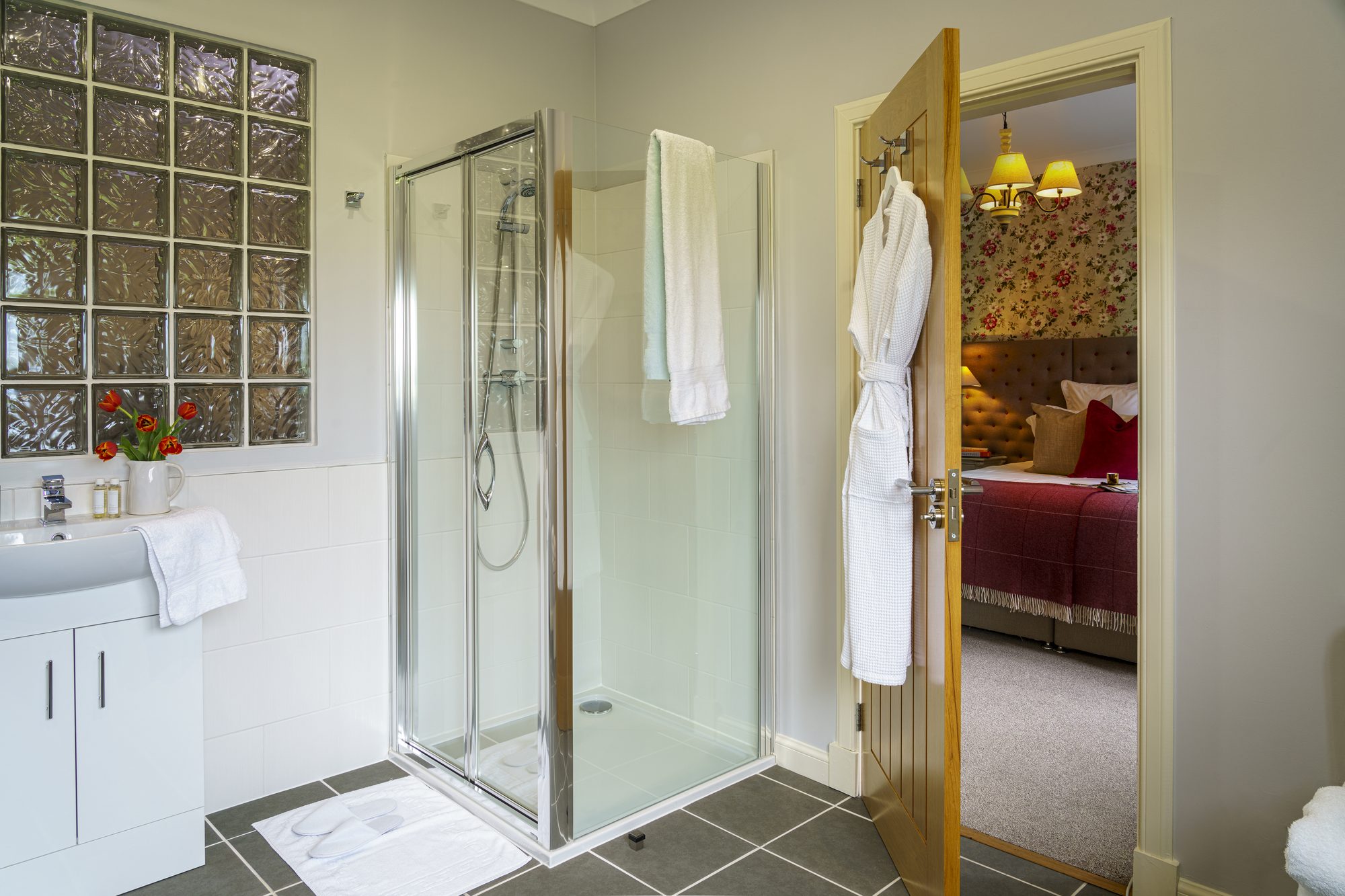 Ensuite shower room with glass-block window and robe on the door at Writers Bow House