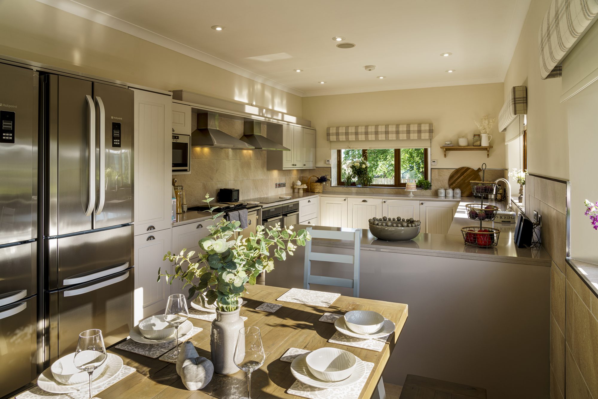 Country kitchen with American fridge, cream cabinets and laid breakfast table at Writers Bow House
