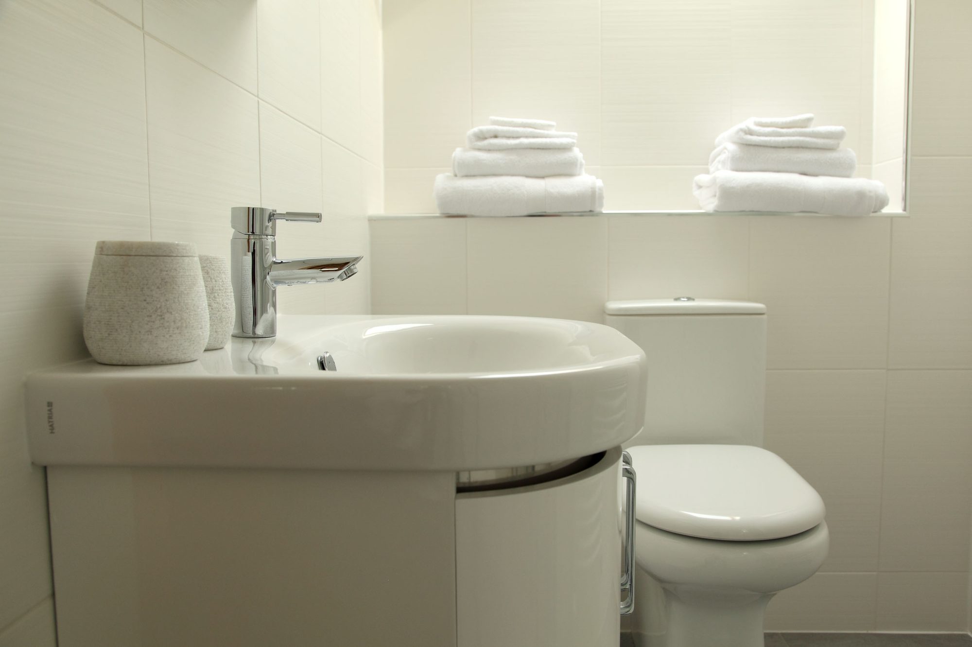 Crisp white ensuite with curved basin, chrome tap and stacked white towels at Writers Retreat