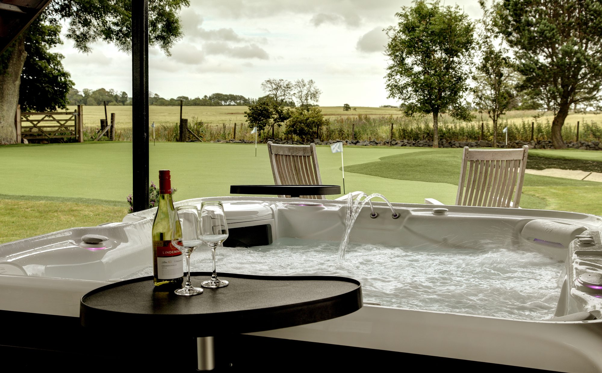 Outdoor hot tub with wine and glasses, looking onto private putting green and Fife fields at Writers Retreat