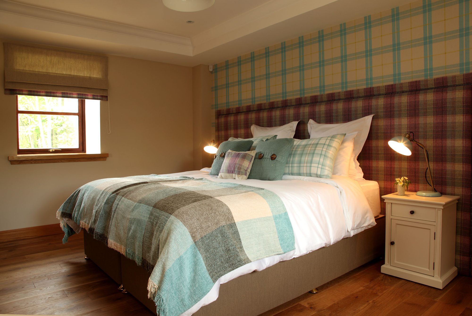 Bedroom with teal and burgundy tartan headboard wall, super-king bed and plaid throw at Writers Retreat