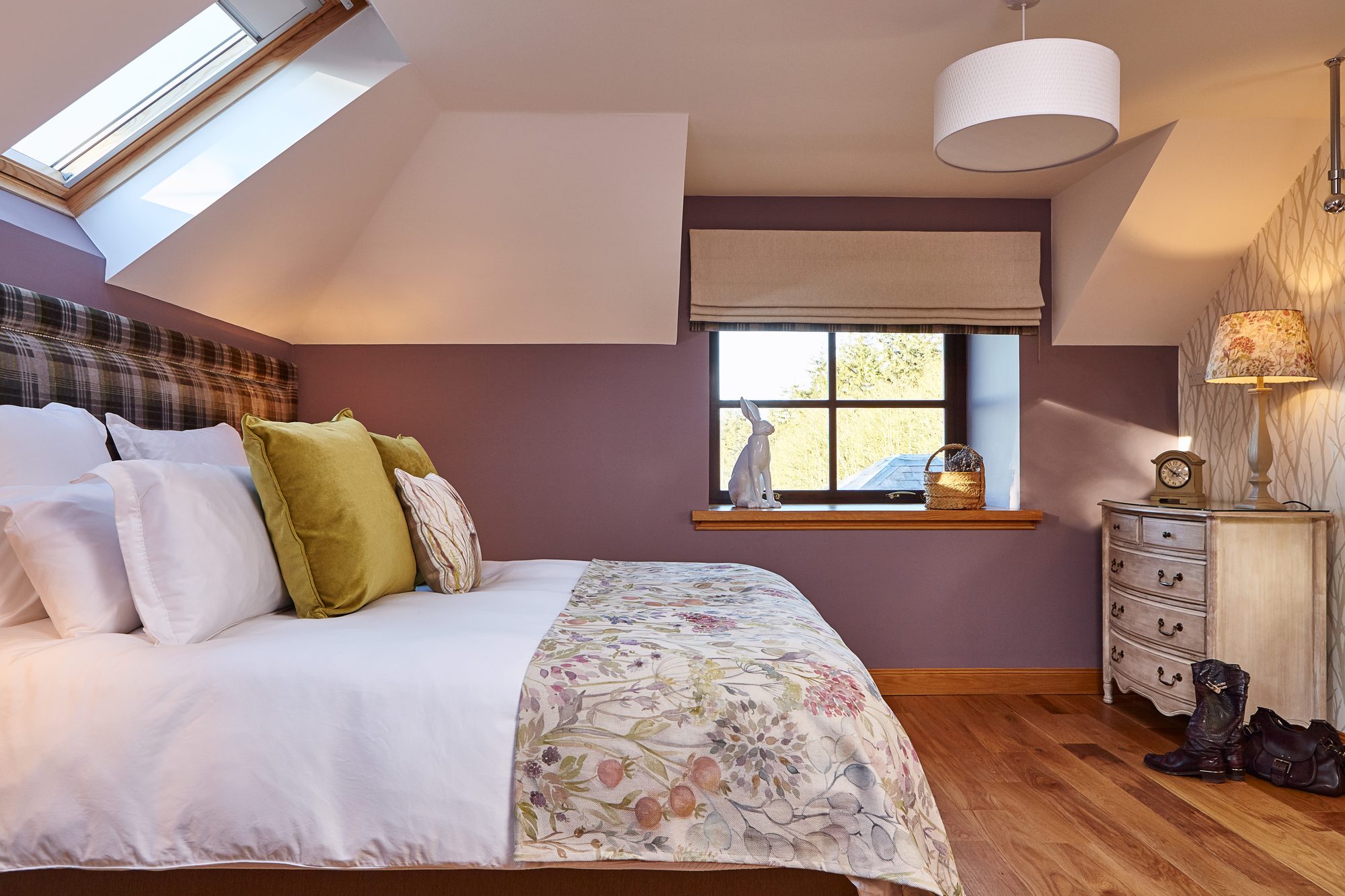 Loft bedroom with plum walls, velux skylight, tartan headboard and floral throw at Writers Round House