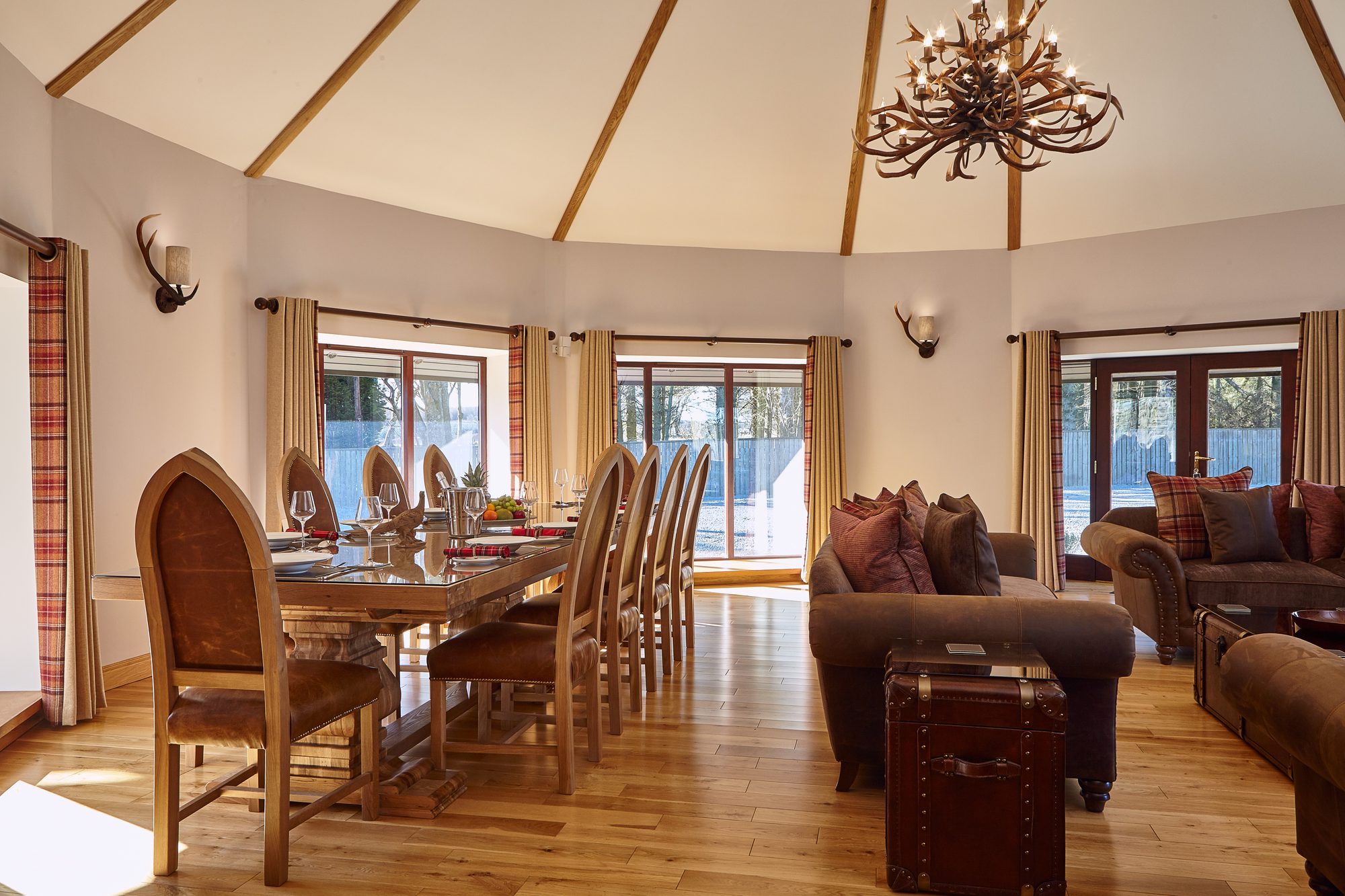 Round dining hall with antler chandelier, leather throne chairs and laid table at Writers Round House