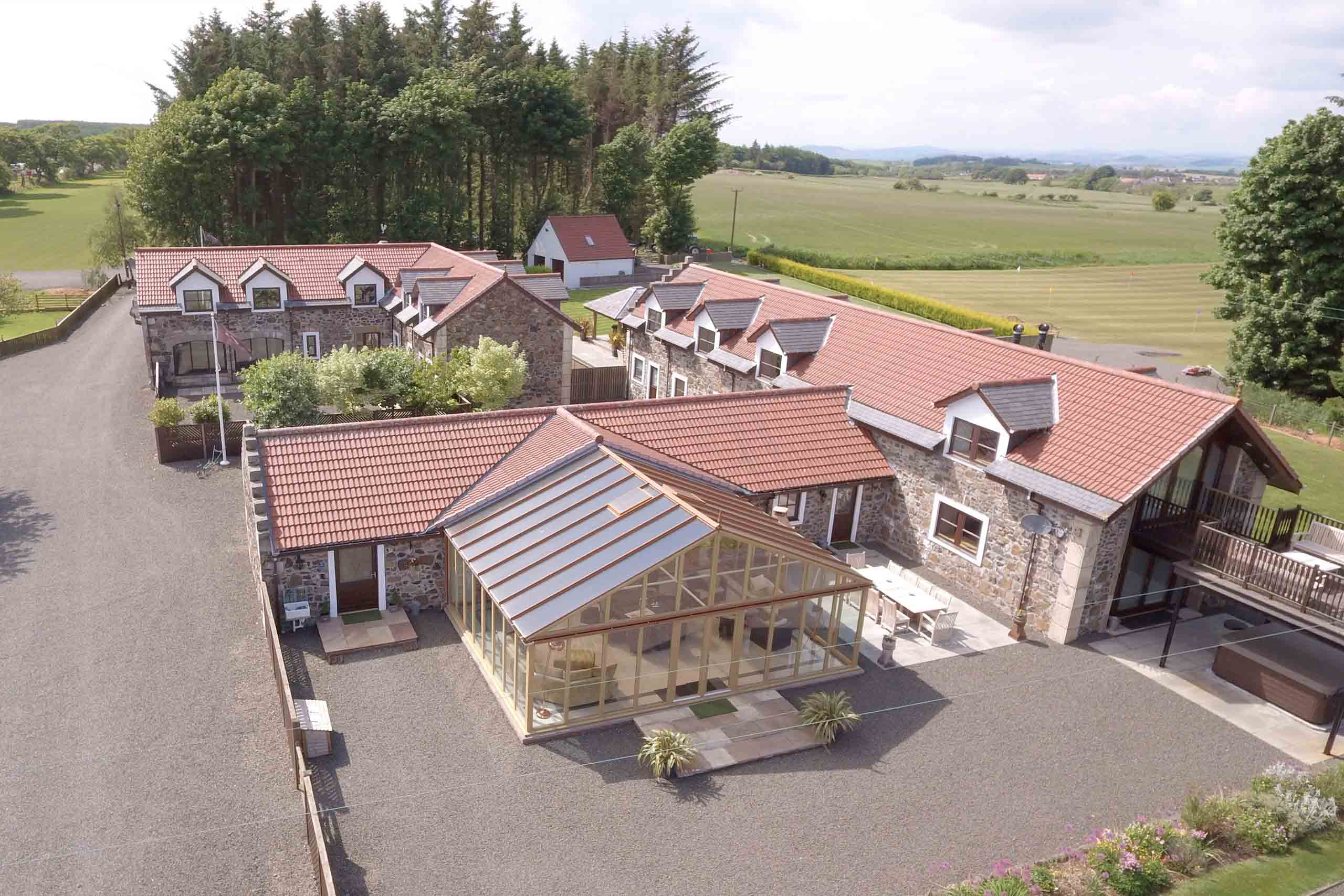Aerial of Writers Round House — stone buildings with glass-roofed pavilion in Fife countryside