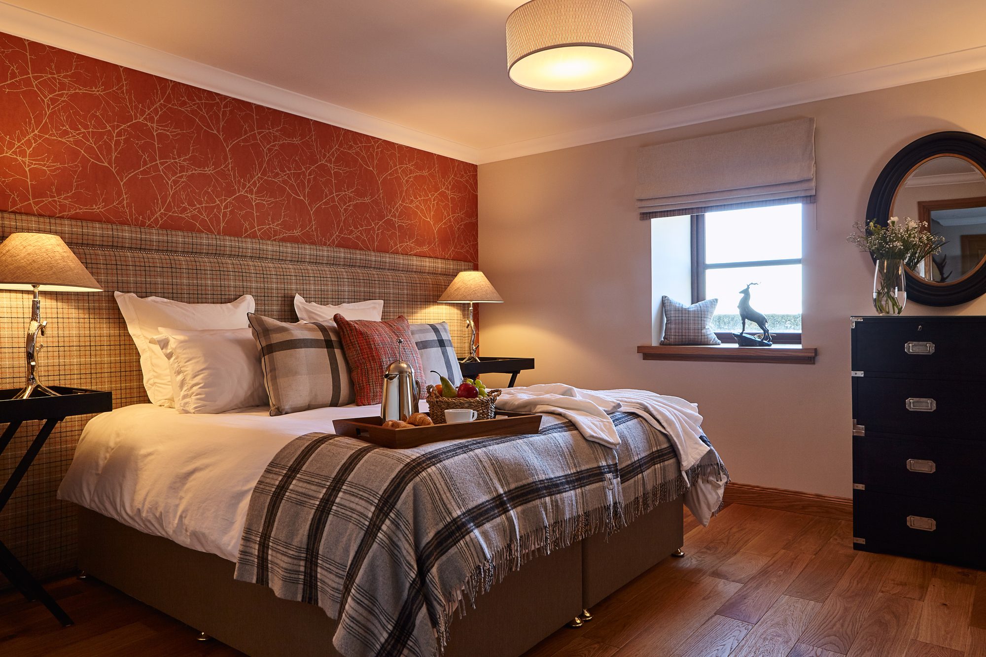 Bedroom with burnt-orange branch wallpaper, tartan headboard and breakfast tray at Writers Round House