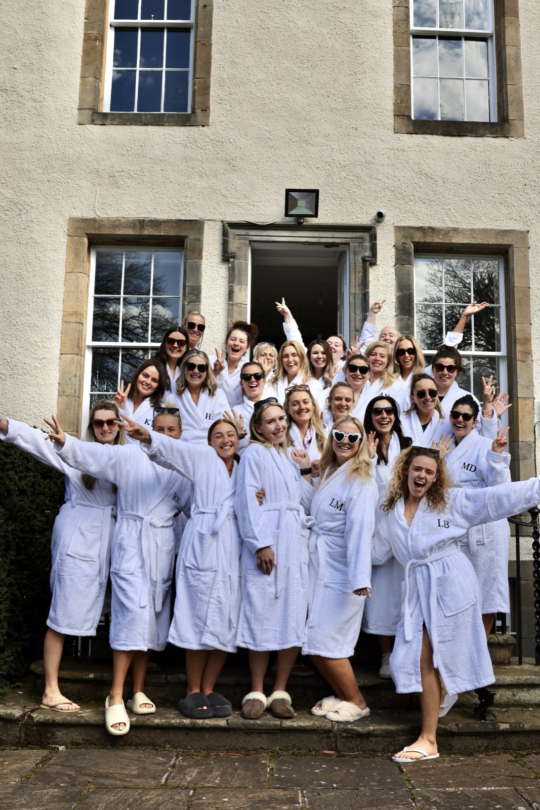 Hen group in matching monogrammed white robes laughing and throwing peace signs on the steps of a Bath country house