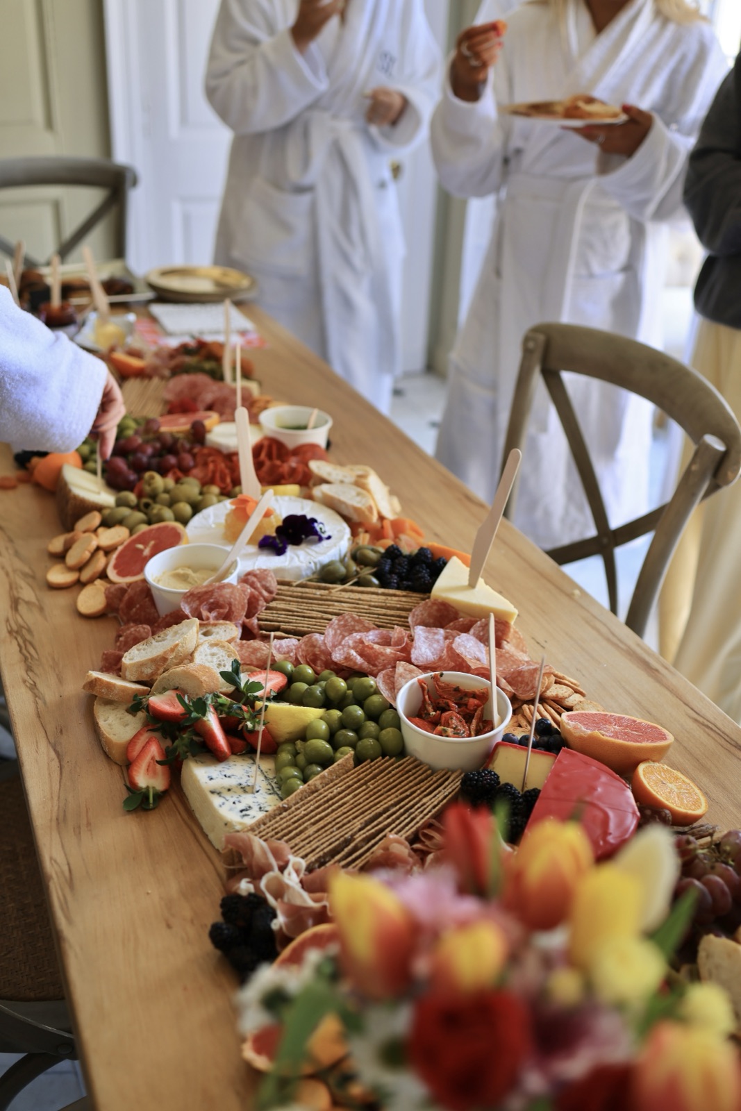 Cotswolds hen party charcuterie grazing table with guests in white robes in the background
