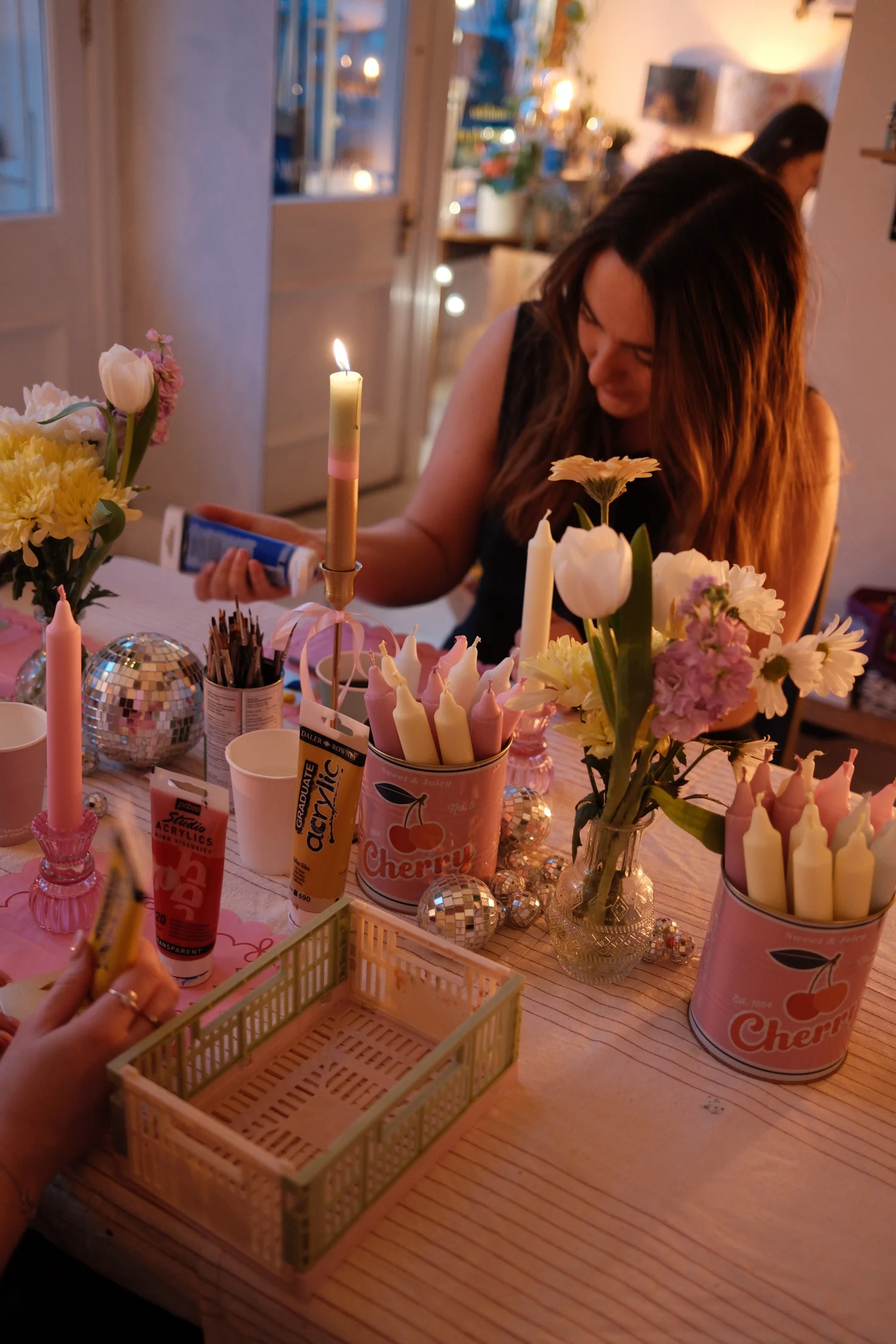 Hen guest hand-painting candles at a Tyninghame Candles workshop, table dressed with flowers, pink tapers and disco balls