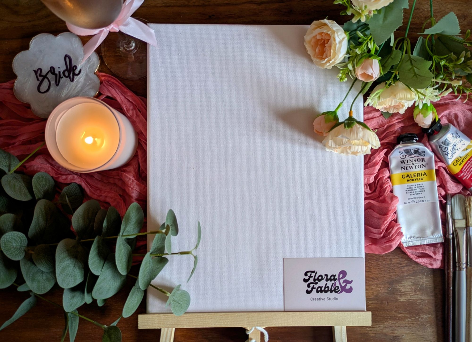 Blank canvas on an easel with paints, brushes and flowers, set up for a Paint the Groom hen party class