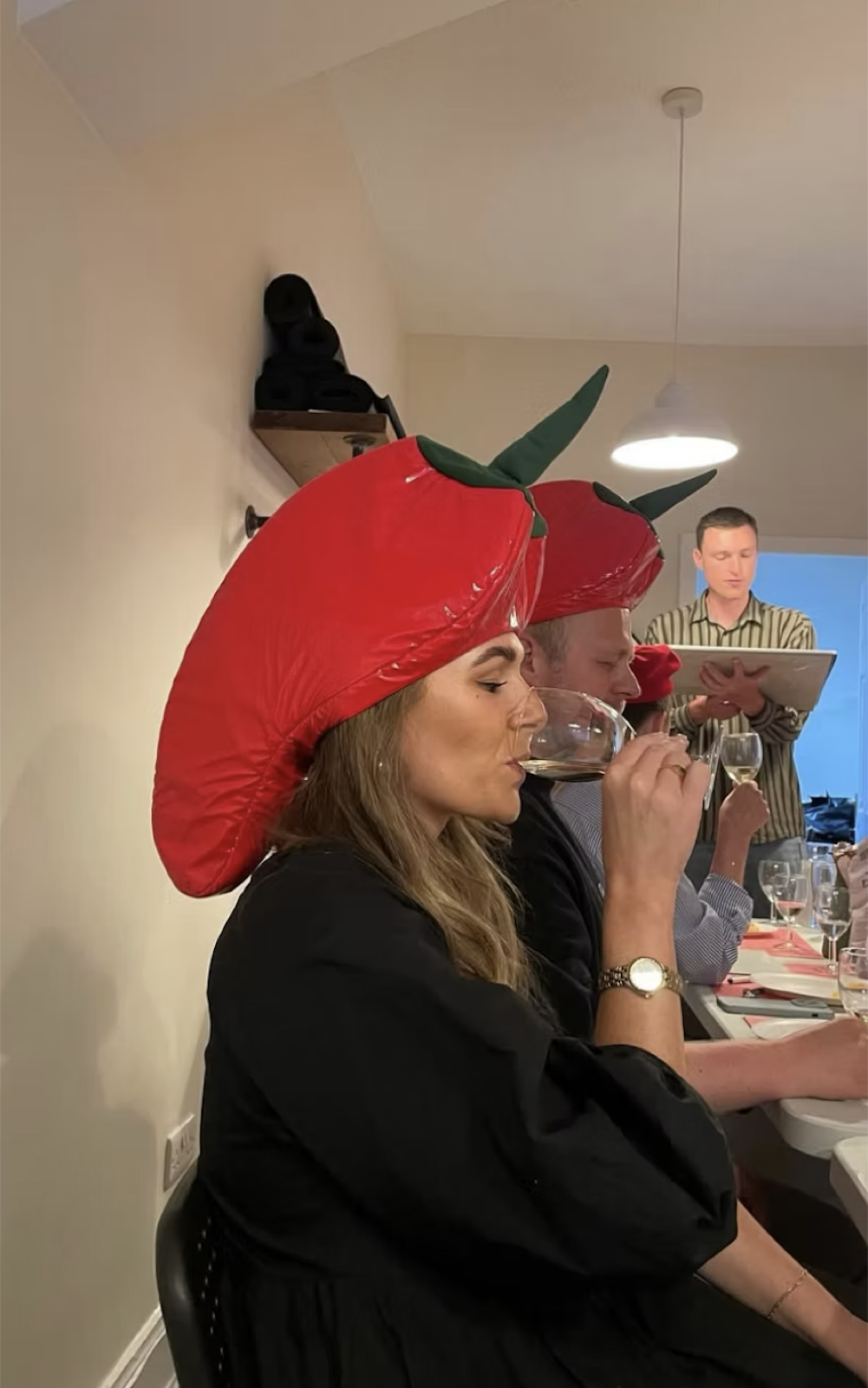 Hen guest in a strawberry-shaped hat sipping at a wine tasting party